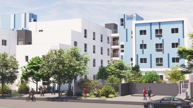 Modern four-story building with white and blue exterior, surrounded by trees and landscaping. People walk and ride bikes along the sidewalk in front of the building, which has a sign reading Daniels Village..
