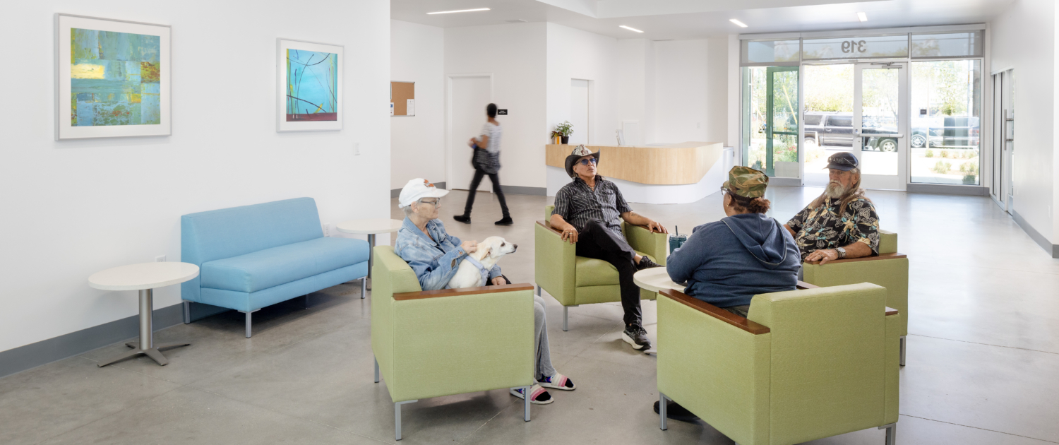 Interior lobby where residents are gathered talking. Four central green chairs surround table.