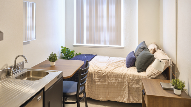 bedroom with small desk, end table and kitchenette