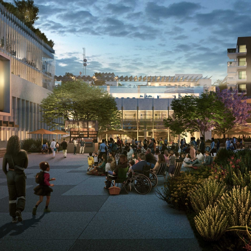 A lively outdoor plaza at dusk with people gathered, some sitting and some walking, facing a large, blurred screen. Modern buildings, greenery, and ambient lighting create a welcoming atmosphere reminiscent of LA Highlights 2021.
